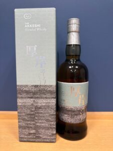 NQe75Oir9wNvrxIOuPDlbvOkDaiDHZL5YSMApV4a お酒買取専門店LIQUORJOYリカージョイ A bottle of Akkeshi Blended Whisky next to its matching gray box on a wooden surface blue backdrop behind them