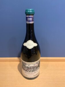 bes75gTBJBD47vTUYRfJtBv3l2alFmeYGO1kRRMK お酒買取専門店LIQUORJOYリカージョイ Wine bottle with a green capsule beige label showing 2023 placed on a wooden table against a blue wall Savigny lès Beaune wine