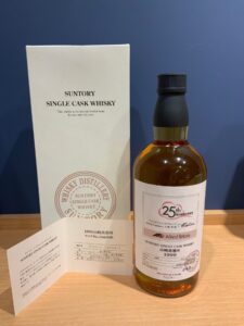 Whisky bottle with black cap beside a white Suntory box on a wooden surface 25th Anniversary label visible on the bottle side panel