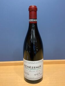Tall wine bottle with red neck foil on a wooden table blue wall background label reads ÉCHÉZEAUX