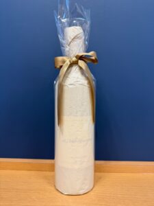 uJ6A2152Fp4JeR5j3HO5g79RwZmHVZj6VZUL5PDO お酒買取専門店LIQUORJOYリカージョイ Gift wrapped bottle with parchment paper and gold ribbon standing on a wooden floor against a blue wall