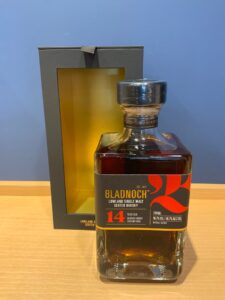 uNIIsDE6Jt6ZI2I1u5yjWo2Jm81uR05KSlTFUsZG お酒買取専門店LIQUORJOYリカージョイ Bottle of Bladnoch 14 year old single malt whisky beside a gray gift box with a yellow interior on a wooden surface