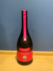 Red wine bottle on a wooden table with a bright pink neck seal and a red label showing 2025