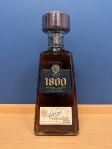 y0ns3X4uTsYDQ9iCHs9jLah0Qt5TbpvFNq4ktmvo お酒買取専門店LIQUORJOYリカージョイ Bottle of 1800 Tequila on a wooden table against a blue wall