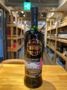 Bottle of dark Scotch whisky with ornate gold label on a wooden counter shop shelves in the blurred background