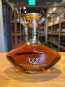 1 お酒買取専門店LIQUORJOYリカージョイ Close up of a Suntory 2000 Millennium Pure Malt Whisky bottle stopper in the foreground with blurred wooden shelves in a shop background