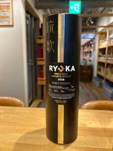 1 お酒買取専門店LIQUORJOYリカージョイ Tall black cylindrical bottle of Ryoka Japanese whisky with a gold decorative stripe on a wooden counter in a shop setting