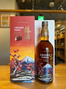 Bottle of Suntory Plum Liqueur beside a red decorative box with Japanese text and mountain blossom artwork