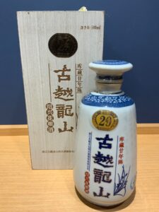 White ceramic liquor bottle with blue decorative patterns and a gold round badge marked 2年 placed beside a light wood box with Chinese characters and a 500ml label