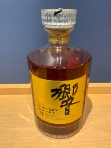 Front view of a Suntory Whisky bottle with a yellow label and clear glass stopper on a wooden surface showing Japanese characters and branding