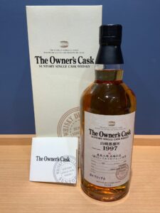 Whisky bottle labeled The Owners Cask beside its white box and a small card on a wooden surface