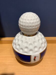 ffNF4RXWQ6VjygKE88XVSCreUF1yQckNRWUezlRM お酒買取専門店LIQUORJOYリカージョイ White ceramic sculpture shaped like a giant golf ball on a blue labeled pedestal featuring a golfer swinging on the label