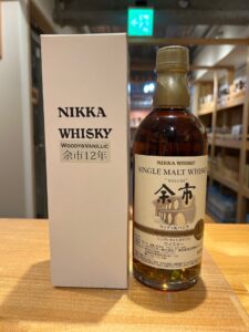 Bottle of Nikka Whisky beside its light colored box on a wooden counter label reads Single Malt Whisky and Woody  Vanillic Japanese text visible