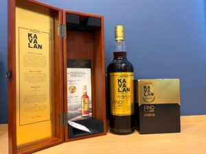 1 お酒買取専門店LIQUORJOYリカージョイ Open wooden display cabinet with Kavalan whisky info panels beside a tall bottle and gold boxes against a blue wall