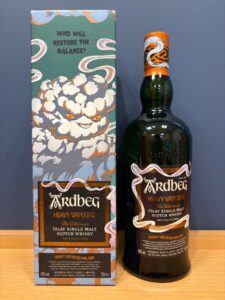 Box and bottle of Ardbeg 'Heavy Vapours' Islay single malt Scotch whisky on a wooden surface with a blue wall backdrop