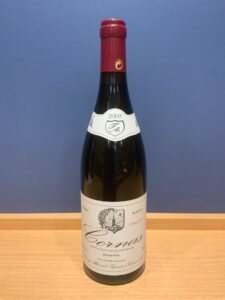 Bottle of red wine with burgundy foil cap 2005 label placed on a wooden surface against a blue wall shows Rhone wine from Cornas