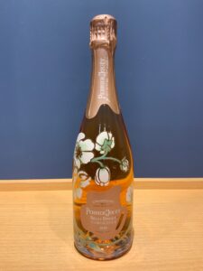 GGhuSVPUeqrPdRvxSk7YKTKalZnHt77y8zCvju9w お酒買取専門店LIQUORJOYリカージョイ Champagne bottle with pink foil and floral artwork Perrier Jouët on a wooden table against a blue wall