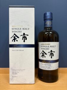 HTiJ3aUX6F1lbGUwXFLb4mMREK1tLlriuK43avea お酒買取専門店LIQUORJOYリカージョイ Box and bottle of Nikka Whisky Yoichi Single Malt Grande Non Chill Filtered on a wooden surface against a blue background showing white box and brown bottle