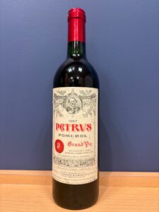Wine bottle labeled Petrus 1987 Pomerol with red foil capsule, ornate vintage label, on a wooden surface.