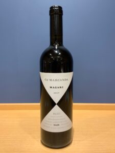 Wine bottle standing on a wooden table with a white label reading CA' MARCANDA MAGARI 2017 on dark glass.