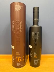 a6eiwG1ByVPyvolhcY0UjdcJ6r3rcT5KNlpBaw7h お酒買取専門店LIQUORJOYリカージョイ Two tall whisky bottles in cylindrical packaging stand on a wooden table a brown tube labeled Ochdamh mòr Islay Single Malt Scotch Whisky edition 162 and a black bottle beside it