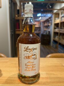1 お酒買取専門店LIQUORJOYリカージョイ Bottle of Longrow peated Campbeltown single malt Scotch whisky on a wooden surface label with a picturesque wineryhouse illustration