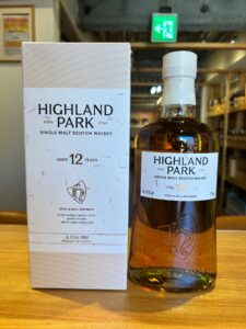 1 お酒買取専門店LIQUORJOYリカージョイ Bottle of Highland Park 12 year old single malt whisky next to its white boxed packaging on a wooden table in a shop setting