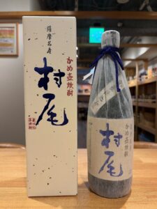 1 お酒買取専門店LIQUORJOYリカージョイ Box and bottle of Japanese sake on a wooden table with blue calligraphy and red stamps on the packaging