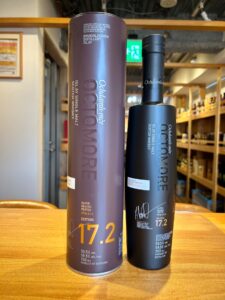 Two tall whisky bottles on a wooden counter in a shop one purple and one black labeled 172 edition of Ochdamh mòr Islay whisky