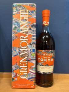 Bottle of Glenmorangie A Tale of Tokyo Highland Single Malt next to a colorful illustrated box with an orange cityscape design on a wooden surface