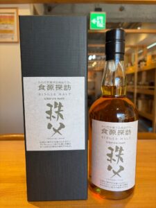 Bottle of Ichiros Malt single malt whisky next to its black gift box on a wooden table label in Japanese and English