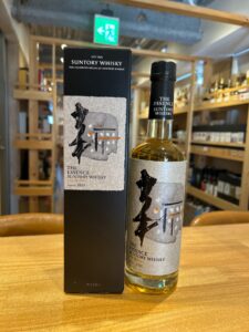 Bottle of The Essence of Suntory Whisky with its black box on a wooden table in a store label features abstract artwork and reads The Essence of Suntory Whisky and Rice Whisky bottled 2020