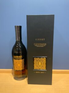 PTtVjrrtqRuHqooktDr4WdzQZdMYYwiPW7RuJ34Q お酒買取専門店LIQUORJOYリカージョイ Glenmorangie Signet whisky bottle beside a tall black gift box on a wooden surface blue wall in the background