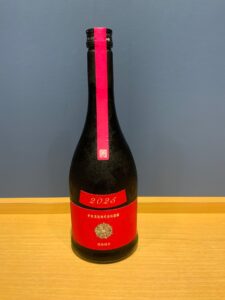 ab330cKm7TOiKRIsx3rU5dO8ShYHWU2JdpCCj6X2 お酒買取専門店LIQUORJOYリカージョイ Dark glass bottle on a wooden surface with a bright pink vertical label and a red 2025 label near the base