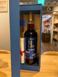 kbQf4ImJPcxDP1stPBvYyK1iXTEQjWIwJrne1mNI お酒買取専門店LIQUORJOYリカージョイ Blue display case holding a Kavalan Solist Vinho Barrique whisky bottle on a wooden table in a shop