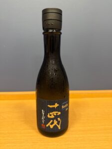 Close up of a dark glass bottle with condensation and a gray cap blue label with gold Japanese characters visible on the body