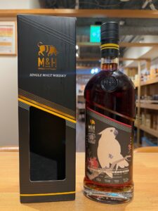 MH single malt whisky bottle with black box on a wooden table packaging in black and gold design with tigerlogo motif