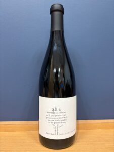 图像 お酒買取専門店LIQUORJOYリカージョイ Dark wine bottle with a pale cream label displaying a circular block of small French text Pinot Noir standing on a wooden surface against a blue wall